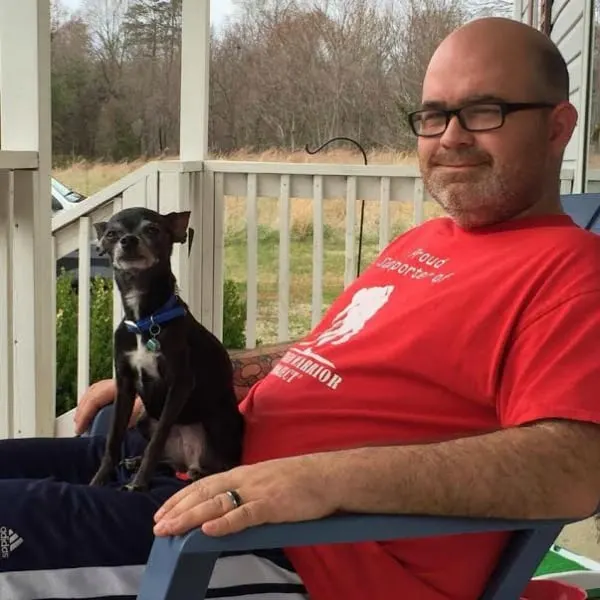 man in red shirt sitting on porch with black and white chihuahua in his lap