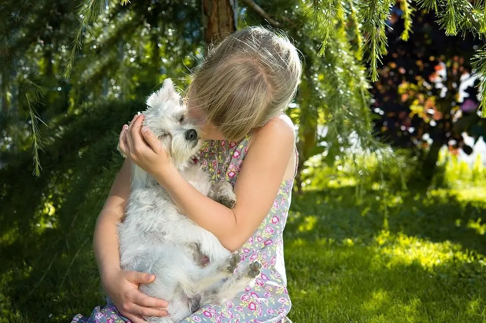 Little girl hugging a white terrier under a tree.