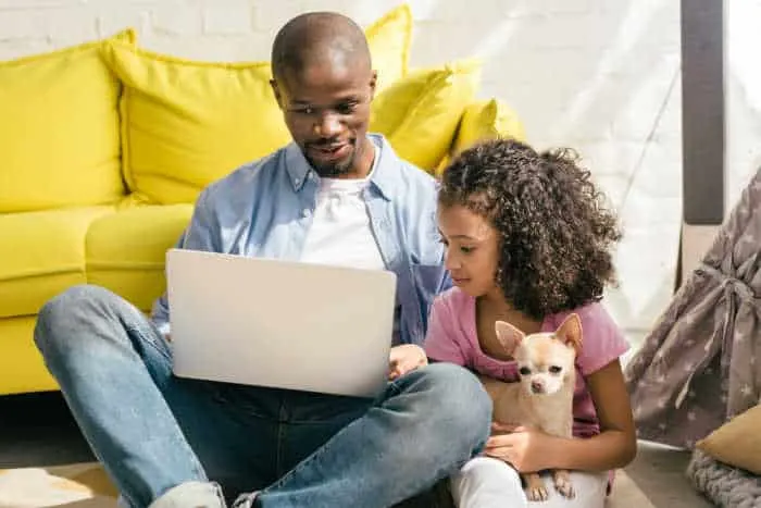 Father and daughter with laptop holding chihuahua.