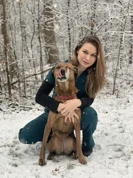 woman kneeling in front of a dog outside in snow