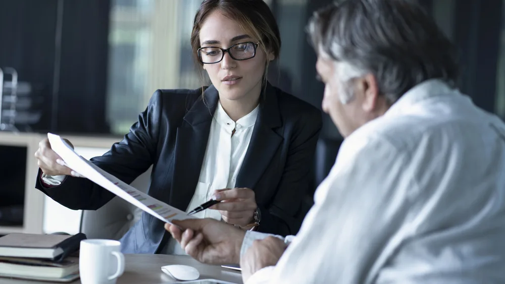 Young female lawyer showing a paper to older man.